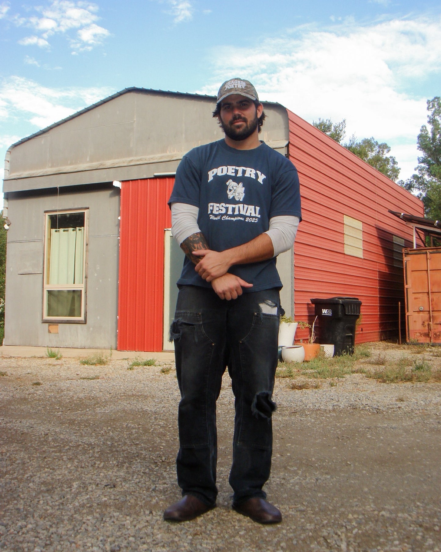 Man wearing a blue t-shirt with 'Poetry Festival' text standing in front of a red building.