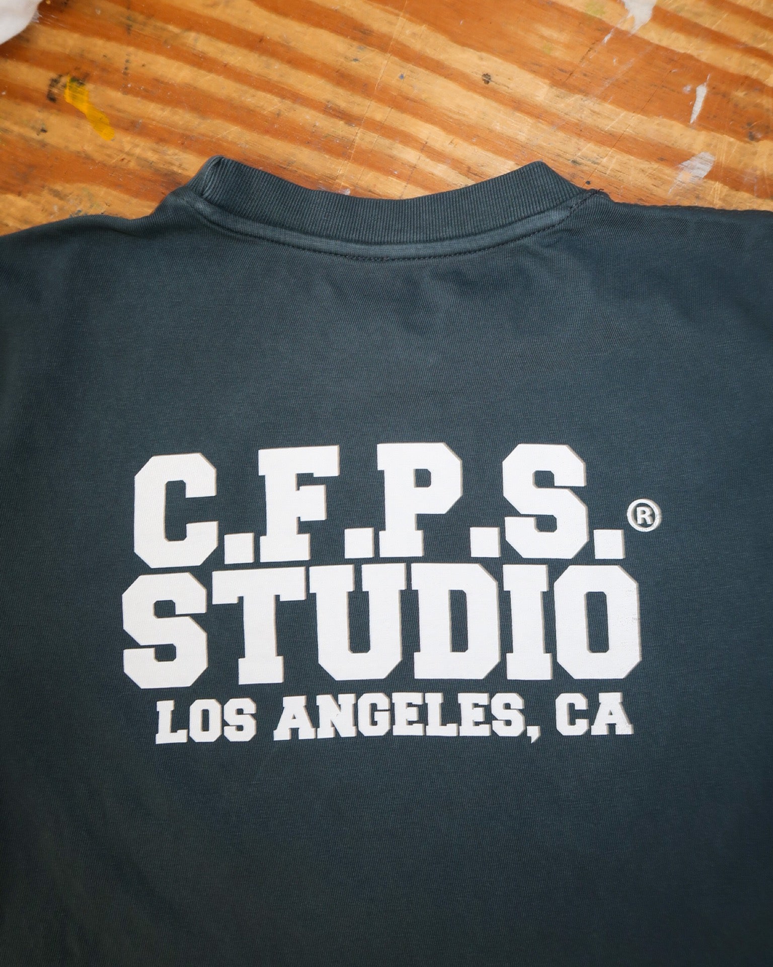 Navy t-shirt with 'C.F.P.S. Studio Los Angeles, CA' text on a wooden surface